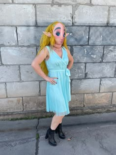 a woman in a blue dress with her face painted like a demon standing next to a brick wall