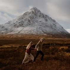 a man and woman dancing in front of a snow - capped mountain on a cloudy day