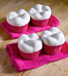 four cupcakes with white frosting on pink napkins sitting on a wooden table