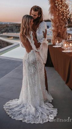 two women in wedding gowns kissing each other on the patio at night with lights behind them