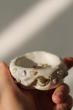 a hand holding a shell shaped object with shells on it's side and pearls in the middle