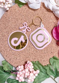 the pink and gold earrings are next to white flowers on a cork board with green leaves