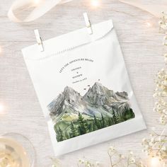 a paper bag with a mountain scene on it next to some wine glasses and flowers