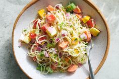 a white bowl filled with pasta and veggies on top of a marble counter