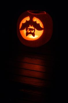 a carved pumpkin sitting on top of a wooden table in the dark with its eyes open