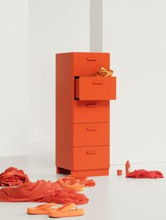 an orange chest of drawers sitting on top of a white floor next to red sheets