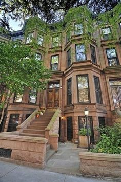 an apartment building with stairs leading up to the front door and trees on either side