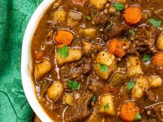 a white bowl filled with stew and carrots on top of a green cloth next to a spoon