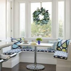 a corner table with blue and white pillows on it in front of a bay window