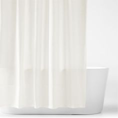 a white shower curtain hanging on the side of a bathtub in front of a white wall