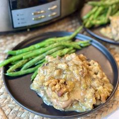 a black plate topped with meat covered in gravy next to green asparagus