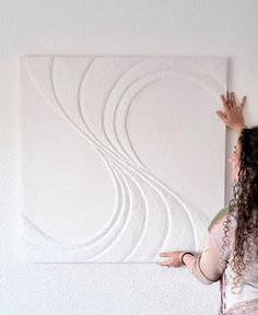 a woman standing in front of a white wall holding her hand up to the ceiling