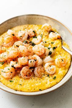 a bowl filled with shrimp and grits on top of a white table next to a fork