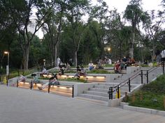 many people are sitting and walking around in the park with stairs lit up at night