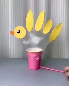 a plastic cup with yellow feathers on it and a hand holding a straw in front of it