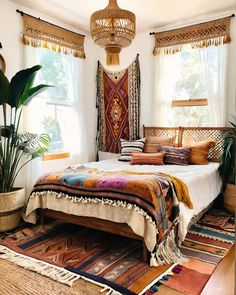 a bedroom with a bed, rugs and potted plants on the floor in front of two windows