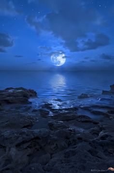 the full moon shines brightly in the sky over the water and rocks at night