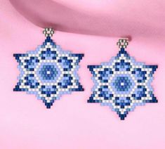 two blue and white beaded earrings hanging from a pink shirt with an ornament design on it