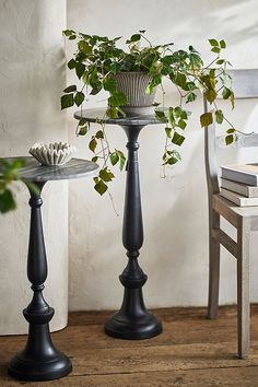 two black pedestals with plants in them on a wooden floor next to a chair