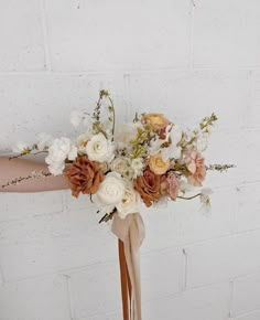 a bridal bouquet with white and peach flowers in front of a brick wall,