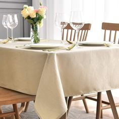 the table is set with plates, glasses and flowers in vases on top of it