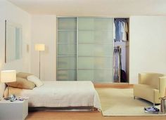 a bedroom with a bed, chair and sliding glass closet doors that open up to reveal a walk - in closet