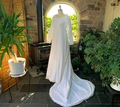 a white wedding dress is on display in front of a brick wall and potted plants