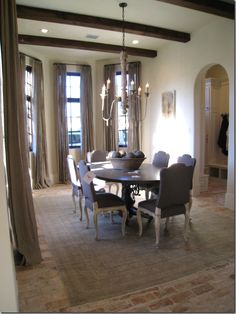 a dining room table with chairs and a chandelier hanging from the ceiling in front of two windows