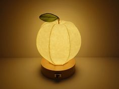 an apple shaped lamp sitting on top of a wooden base with a green leaf in the center