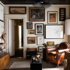 a living room filled with lots of framed pictures on the wall above a leather chair