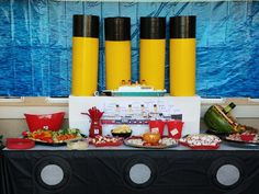 a table topped with lots of food next to tall yellow vases filled with flowers