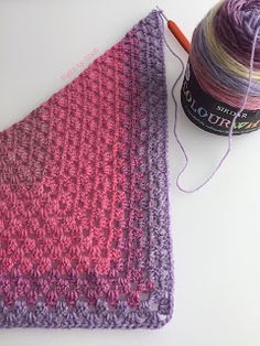 a pink and purple knitted blanket next to a ball of yarn with a skein of thread