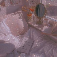 a book is laying on a bed with white sheets and sparkles all over it