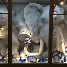 an elephant display in a store window with blue and white plates on the shelf next to it