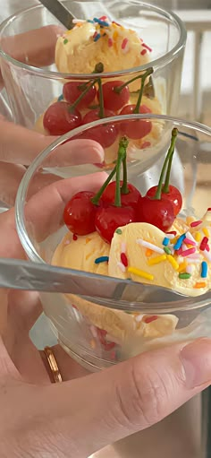 two small desserts in glass bowls with toppings on them are being held by someone's hands