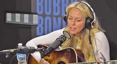 a woman sitting in front of a microphone with headphones on while playing an acoustic guitar