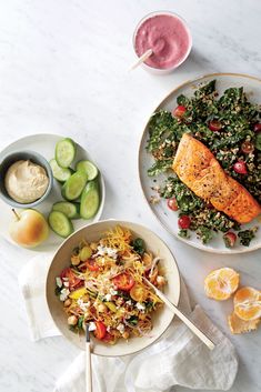 two plates filled with food next to bowls of fruit and vegetables on a white table