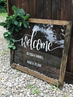 a welcome sign on the side of a wooden fence with greenery hanging from it