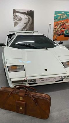 a white sports car parked next to a suitcase in a room with posters on the wall