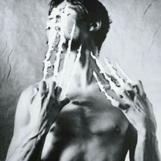 a shirtless man is holding his hands over his face and covering his mouth with strings