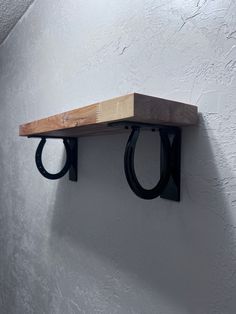 a wooden shelf with two black rings hanging from it's sides against a white wall