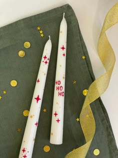 two white candles sitting next to each other on a green cloth with gold confetti