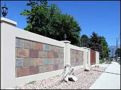 a stone wall next to a sidewalk in front of a tree and lampposts