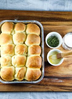 a baking pan filled with rolls and dips on top of a wooden cutting board