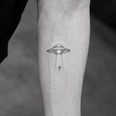 a small tattoo on the leg of a person with an alien ship flying above it