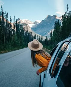 a woman leaning out the window of a car on a road with mountains in the background