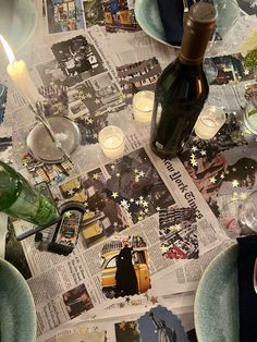 a table topped with plates and candles next to a bottle filled with wine on top of a newspaper