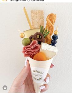 a person holding an ice cream cone filled with different types of food and toppings