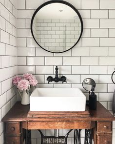 a bathroom sink sitting under a mirror next to a table with flowers on top of it