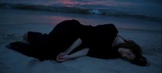 a woman laying on the beach at night with her head down and eyes closed, wearing a black dress